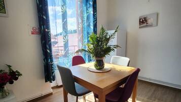 Et spiseområde med et træbord, fire stole, en potteplante og et vindue med gardiner.
