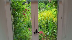 Una porta amb un tirador negre, que dona a un jardí ple de plantes i flors diverses.