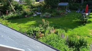 Un jardí exuberant amb un hivernacle, un porxo i una zona d'estar amb cadires i una taula.