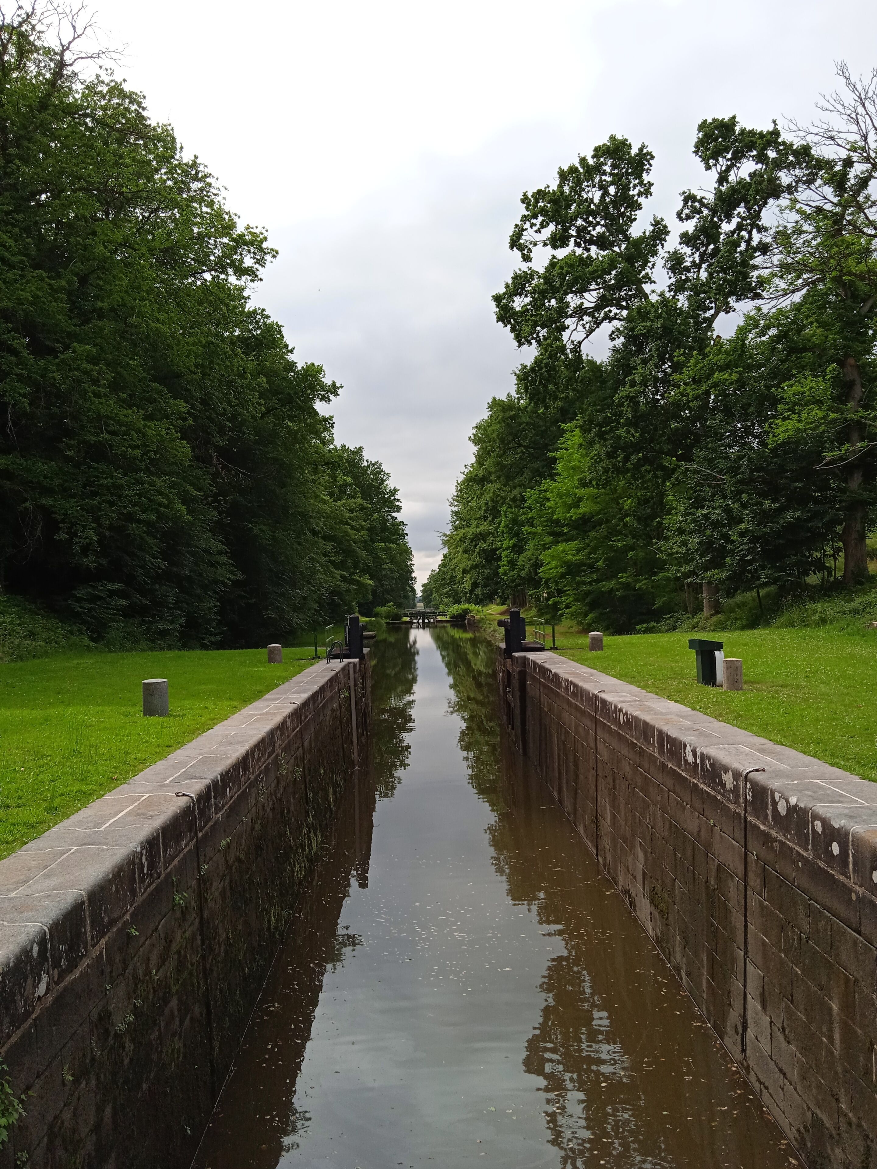 A canal flanked by stone walls and lush greenery, leading to a distant bridge.