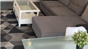 A compact living space with a kitchenette, a grey sofa, a glass coffee table, and a small potted plant. - Maison de 50m2 Avec Piscine Commune (Fréjus)