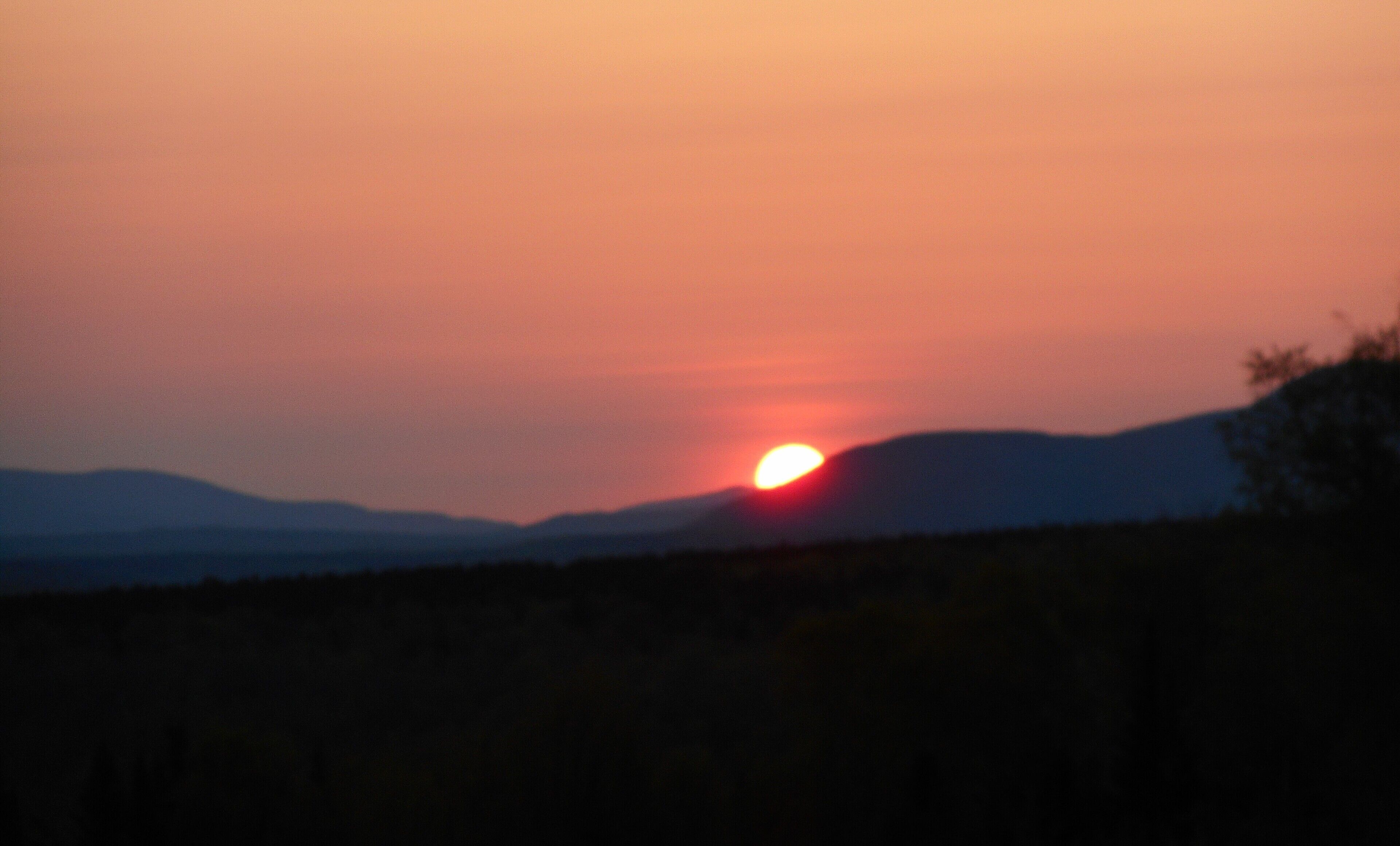Een zonsondergang boven een bergachtig landschap met een heldere lucht.