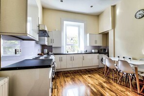 A modern kitchen with a dining area, wooden flooring, and a window providing natural light.