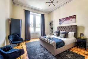 A bedroom with a bed, a chair, a nightstand, a window with curtains, and a wall-mounted picture.