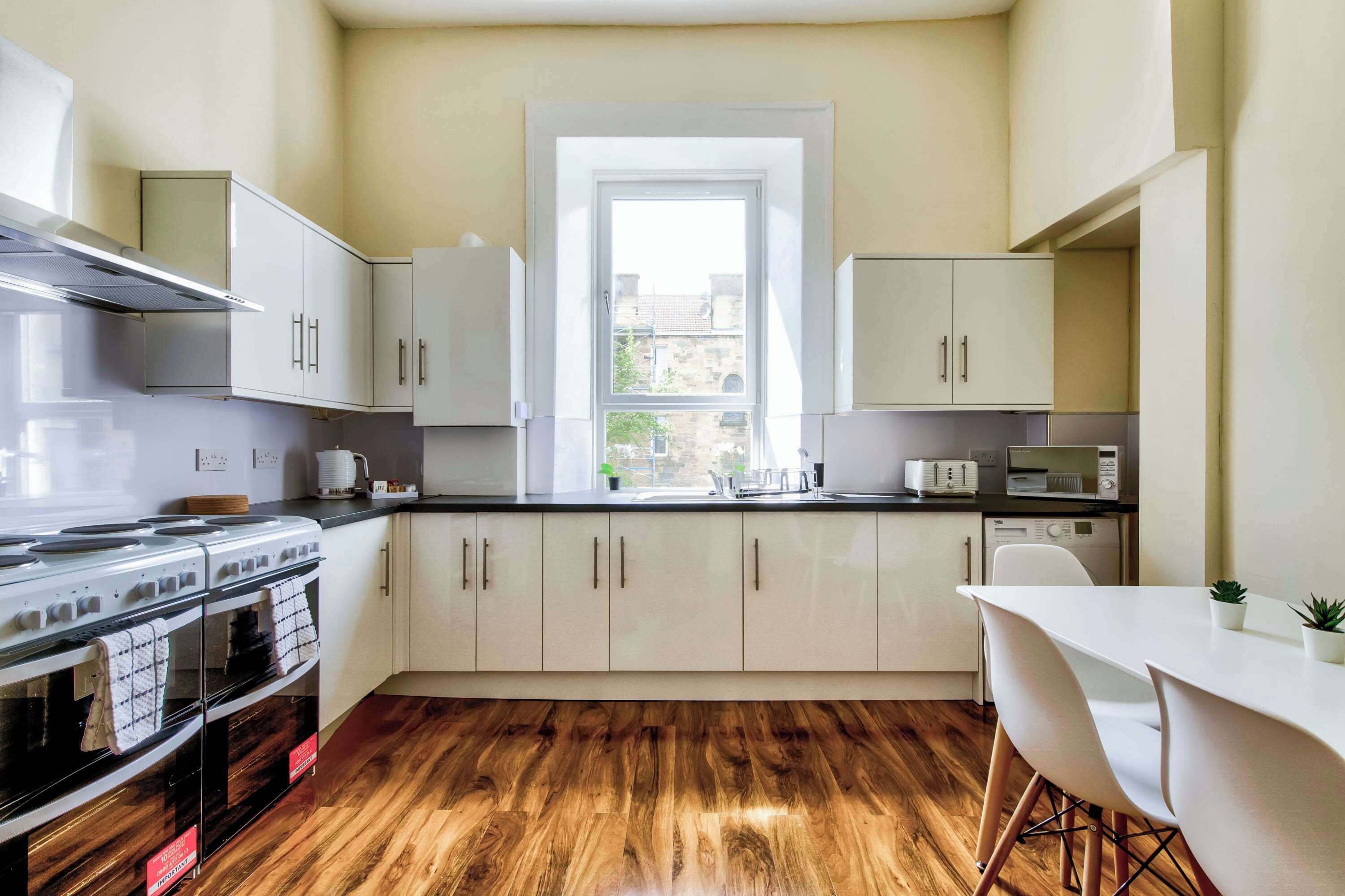 A modern kitchen with white cabinets, a stove, and a window.