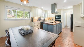 A modern kitchen with white cabinets, a central island, and a dining area with a wooden table. - TOP-RATED! HOT TUB, KAYAKS, FISHING, BOAT DOCK! Granbury Paddle and Play Escape! (Granbury)
