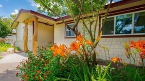 A house with a brick exterior, a porch with wooden columns, and a garden with orange lilies and red flowers. - TOP-RATED! HOT TUB, KAYAKS, FISHING, BOAT DOCK! Granbury Paddle and Play Escape! (Granbury)