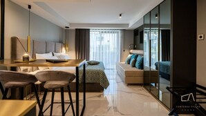 Una camera d'hotel moderna con divano, angolo ristoro e un grande specchio.