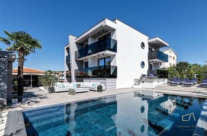 Eine moderne Villa mit Pool, Sitzgelegenheit im Freien und strahlend blauem Himmel.