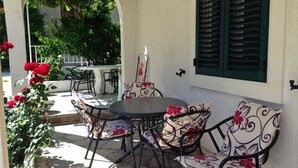 Un patio al aire libre con una mesa redonda y cuatro sillas, rodeado por un muro blanco con contraventanas verdes.