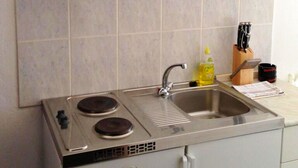 Une cuisine compacte équipée d’une cuisinière intégrée, d’un évier et d’une étagère au-dessus pour ranger la vaisselle et les récipients.