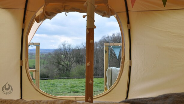 Een rond raam in een tent met uitzicht op een grasveld en bomen.
