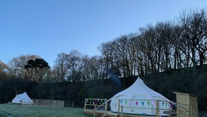 Een camping met een grote witte tent en een kleinere houten constructie.