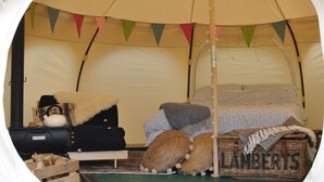 Een gezellig ingerichte tent met een bed, kussens, een deken en een mandje met de tekst 'LAMBER'S'.