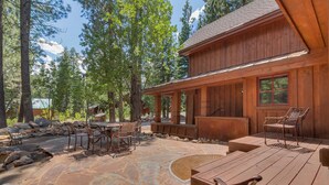 Une cabane en bois dotée d’un patio avec un sol en pierre, du mobilier d’extérieur et une vue sur les arbres environnants.