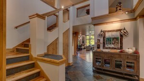 Un hall d’entrée spacieux, agrémenté d’un escalier en bois, d’une commode rustique et offrant une vue sur le salon.