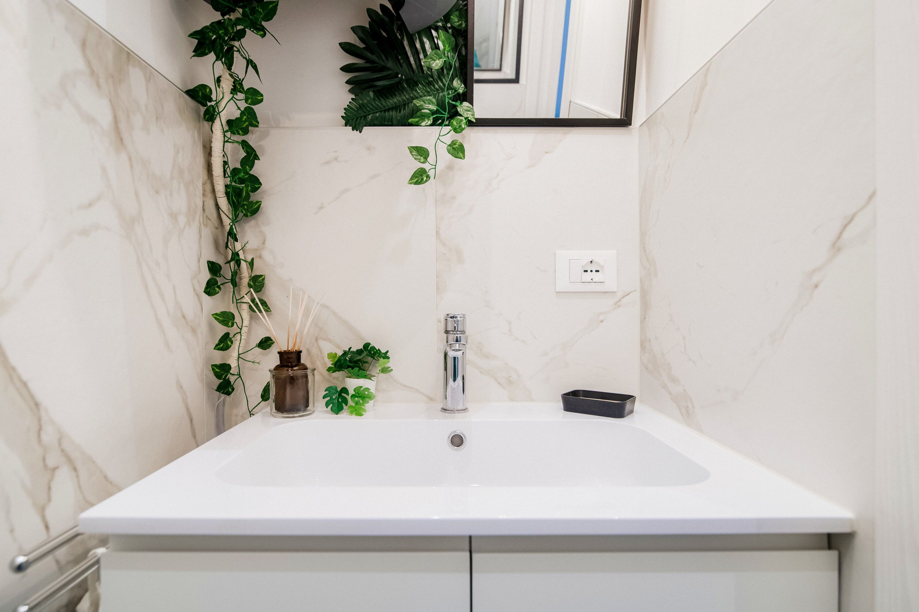 Un bany amb un lavabo de marbre blanc, un aixeta, una petita planta i un mirall.