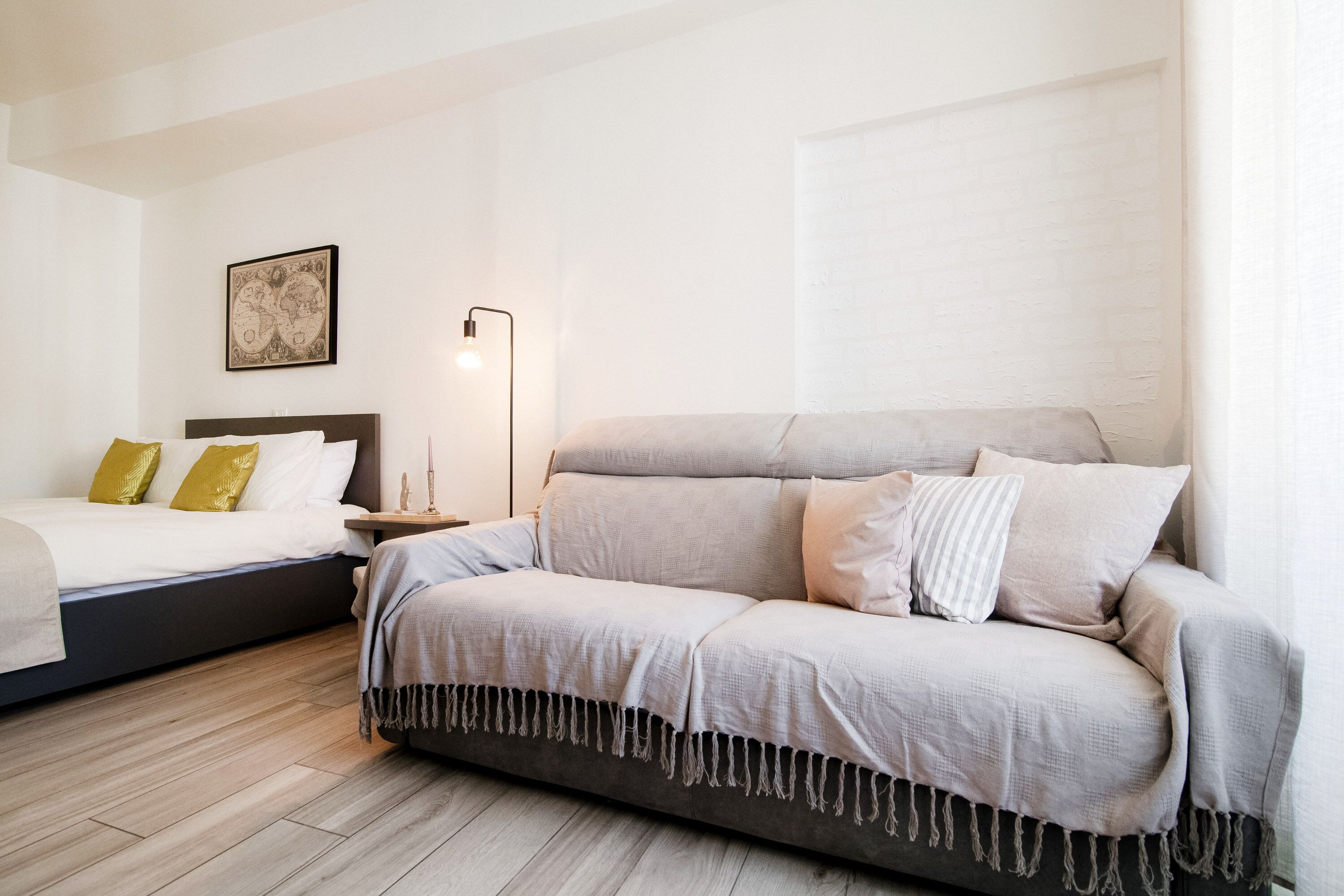A bedroom with a bed, a sofa, a bedside table, a lamp, and a wall-mounted artwork.