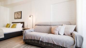 Un dormitorio con una cama, un sofá, una mesita de noche, una lámpara y una obra de arte colgada en la pared.