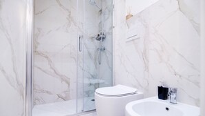 Ein modernes Badezimmer mit einer gläsernen Duschkabine, einer weißen Toilette und einem Waschbecken mit schwarzem Seifenspender.