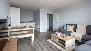 A modern living room with a grey sofa, a wooden coffee table, and a kitchen area with a dining table and chairs. - Modern 1BED Central Birmingham Apartment- Sleeps 4 (Birmingham)