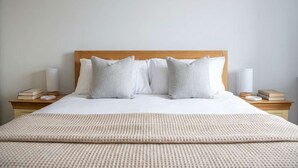 A neatly made bed with a wooden headboard, white bedding, and two bedside tables with lamps and books. - Modern 1BED Central Birmingham Apartment- Sleeps 4 (Birmingham)