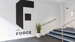 A staircase with a metal handrail, a potted plant, and a wall with a large black letter 'F' and the text 'THE FORGE'. - Modern 1BED Central Birmingham Apartment- Sleeps 4 (Birmingham)