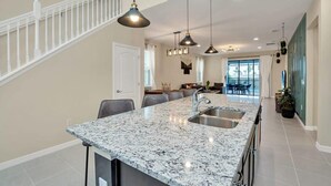 Una cocina con encimera de granito, pileta de acero inoxidable, iluminación colgante y una escalera.