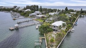 An aerial view of a waterfront property with multiple docks, a large house with a balcony, and a small boat docked nearby. - Boaters Paradise  ***Palm Point*** Little Gasparilla North Canal on the POINT (Placida)
