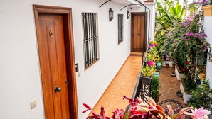 A narrow, tiled corridor with a wooden door and a window with metal bars. - Marbella Village | Studio with balcony (Marbella)