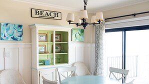 A dining area with a round table and four chairs, a cabinet with green doors, and a sign on the wall that reads "BEACH". - 3 Bed~3 Bath~Sleeps 8~Duneridge Condo~Wrightsville Beach, NC (Wrightsville Beach)