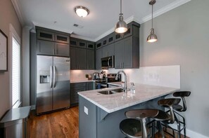 A modern kitchen with grey cabinets, stainless steel appliances, a marble island, and bar stools. - New Nashville Condo with 2 King beds, walk to bars (Nashville)