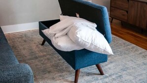 Ein kleines Bett mit dunkelblauer Kopfteil in einem Zimmer, das einen Holzkasten und einen grauen Teppich zeigt.