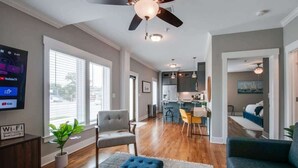 Ein modernes Wohnzimmer mit Fernseher, Sitzmöbeln und Deckenventilator.