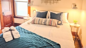 A neatly made bed with a striped blanket and pillows, a bedside table with a lamp, and a wall art piece.
