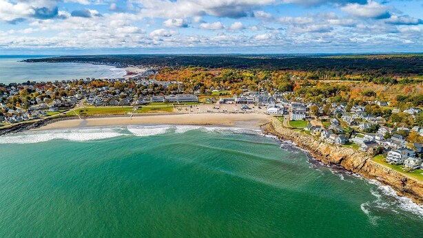An aerial view of a coastal town with a beach, houses, and a rocky shoreline.