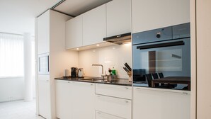 A modern kitchen with white cabinetry, a black refrigerator, and a dining area with a table and chairs.