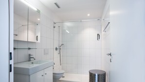 A modern bathroom with a glass shower enclosure, a white sink, and a toilet.