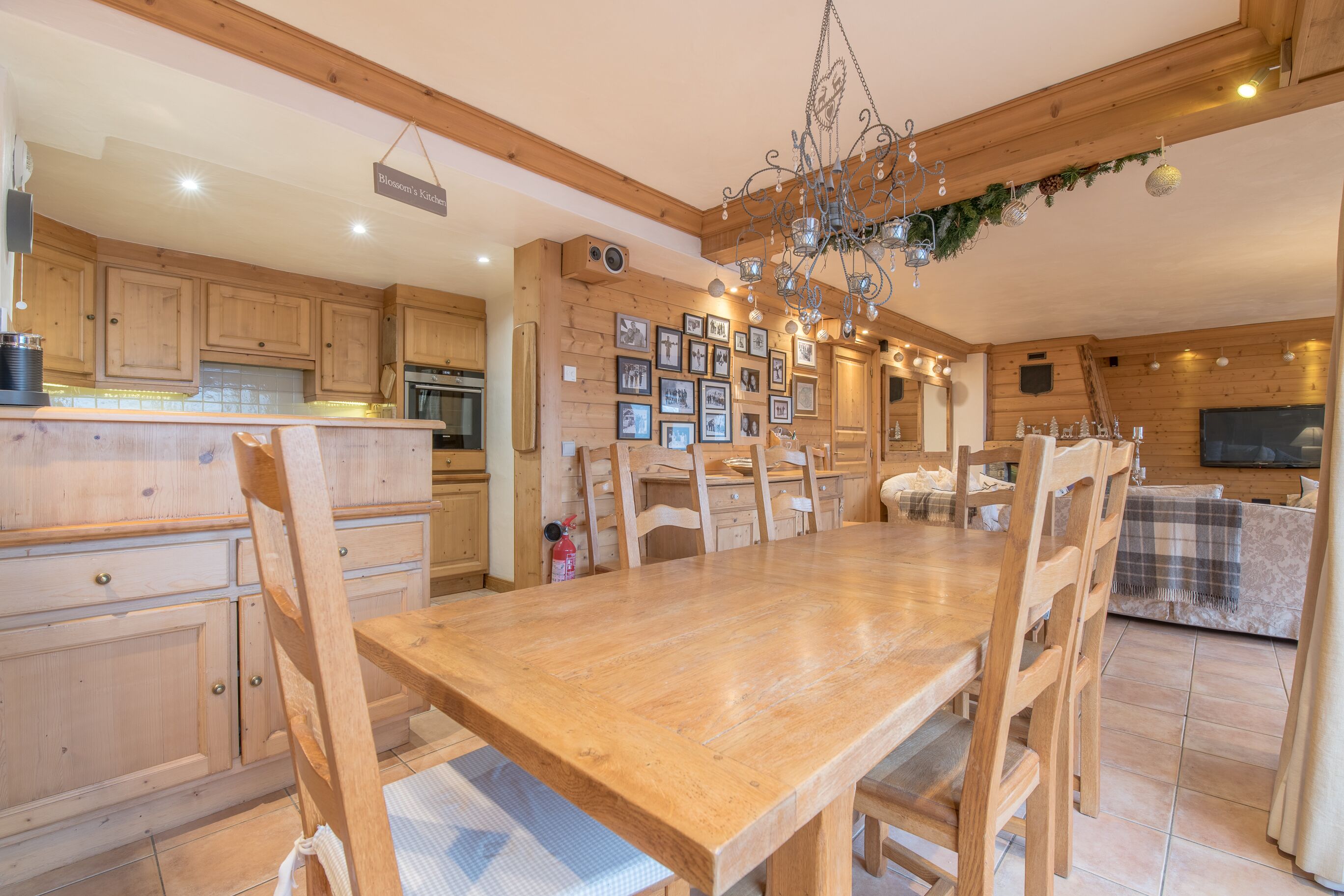 Une table à manger en bois, des chaises, un lustre et des tableaux encadrés accrochés au mur.