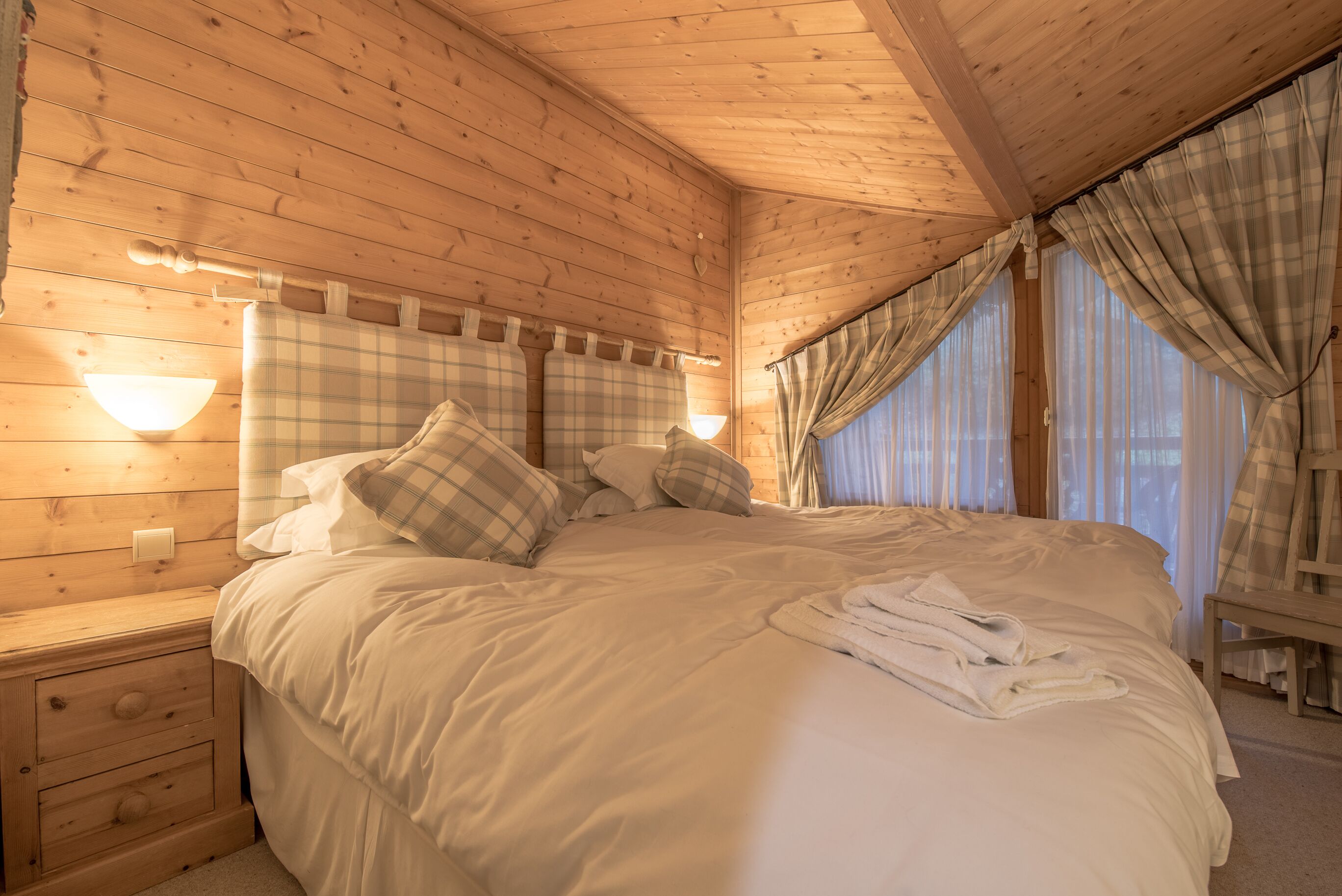 Une chambre dans une cabane en bois, avec un lit, des tables de chevet et une fenêtre avec des rideaux.