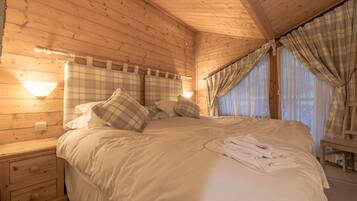 Une chambre dans une cabane en bois, avec un lit, des tables de chevet et une fenêtre avec des rideaux.