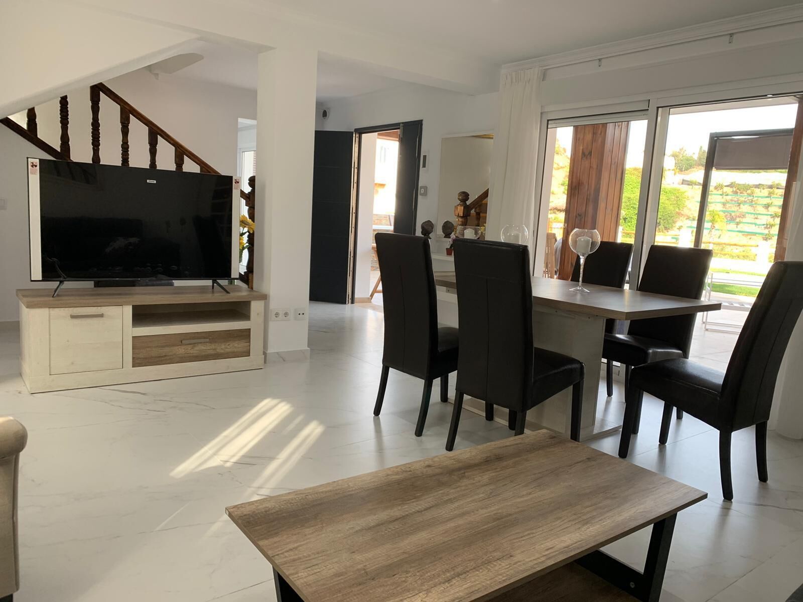 Een moderne woonkamer met een flatscreen televisie, een houten entertainmentkast en een eethoek met een tafel en stoelen.