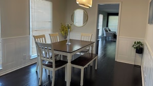 Een eethoek met een houten tafel en witte stoelen, een vaas met bloemen en een hanglamp.