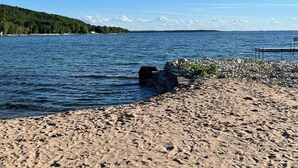 Ein Strand mit felsigem Ufer, einer Anlegestelle und einem bewaldeten Hügel im Hintergrund.