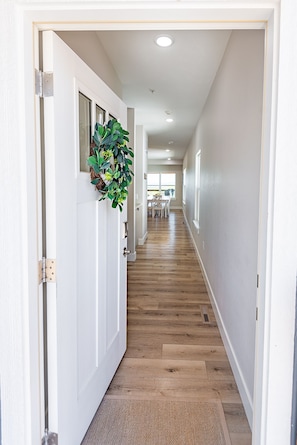 A hallway with wooden flooring, white walls, and a door with a plant decoration.
