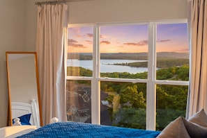 A bedroom with a large window, a bed, a bedside table, and a mirror.