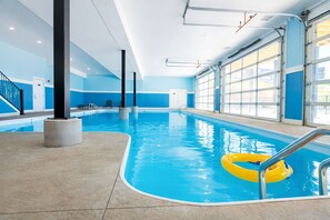 An indoor swimming pool with clear blue water, a yellow float ring, and a staircase leading to a door.