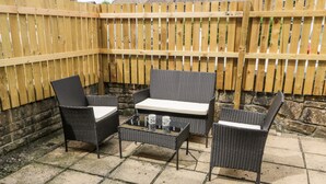 Un patio con mobili in vimini, un tavolo e una recinzione in legno.
