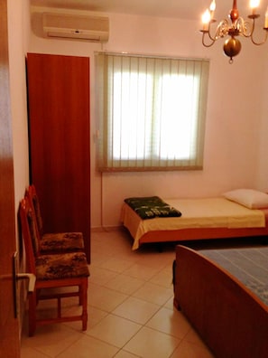 A bedroom with a bed, a chair, a window with blinds, and a chandelier. - A3 - apt w. Patio, 3 min Walking From the Beach (Dugi Rat)
