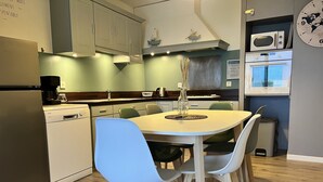 A modern kitchen with a round dining table, light-colored chairs, and a microwave above the counter. - Bélicine, seafront apartment for 5 people  (LE CROTOY)